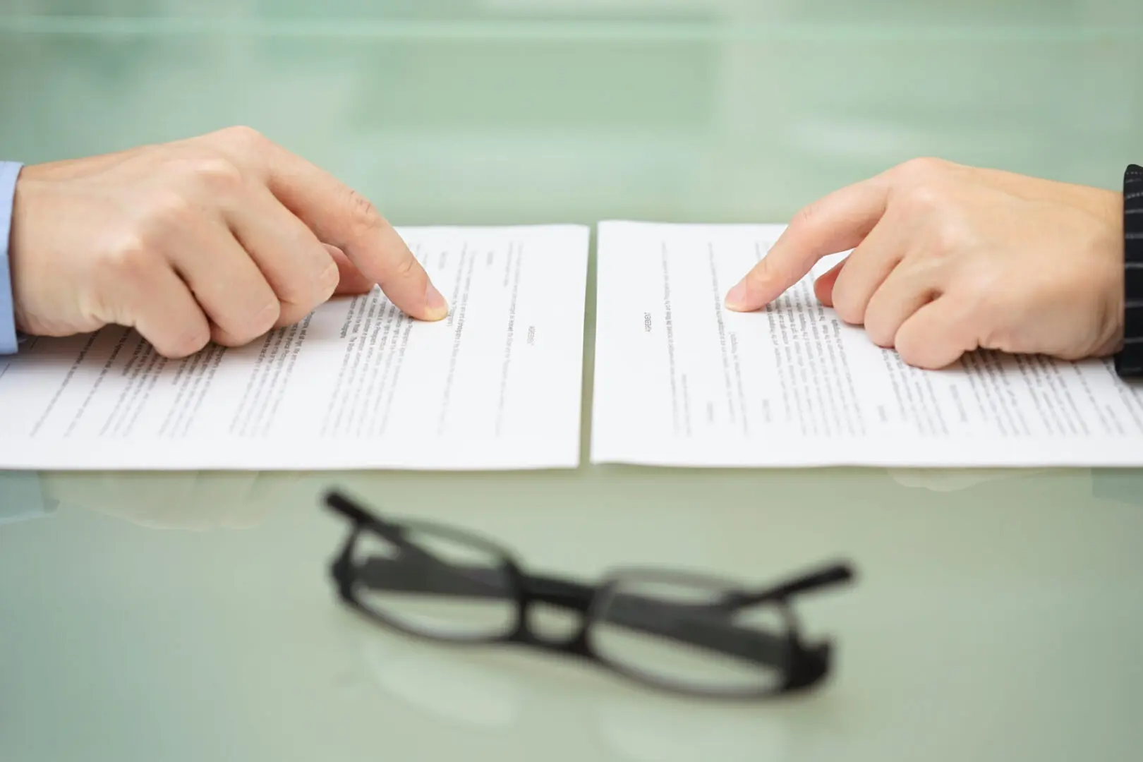 A person is reading a paper with glasses on the table.